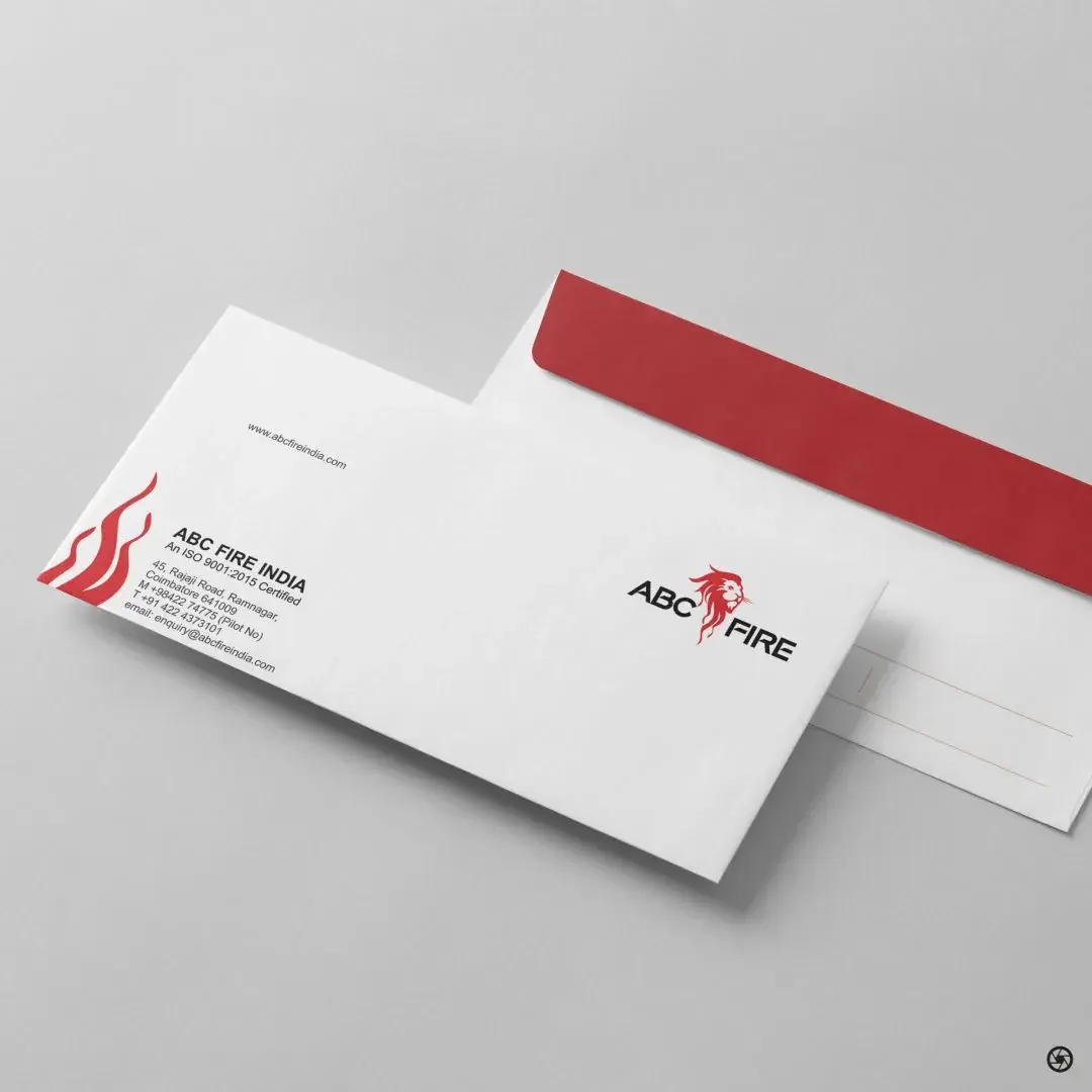 ABC Fire - DL envelope with the company address block on the left, www.abcfireindia.com top centre, and the lion-and-wordmark on the right, with a matching red envelope behind