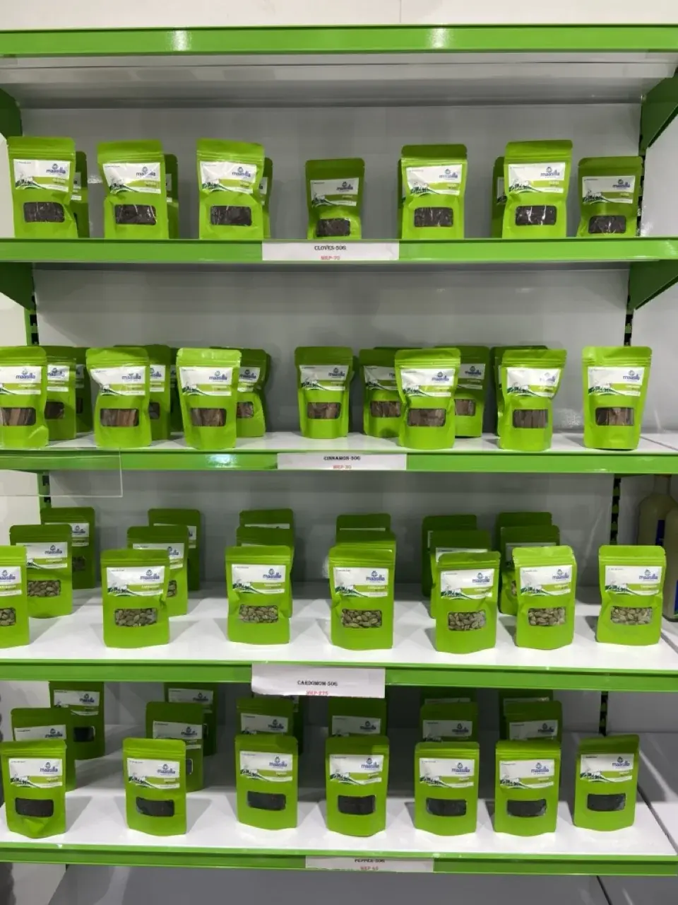 Maasilla spice wall - cloves, cinnamon, cardamom, and pepper in branded green resealable pouches, shelved on green retail racks
