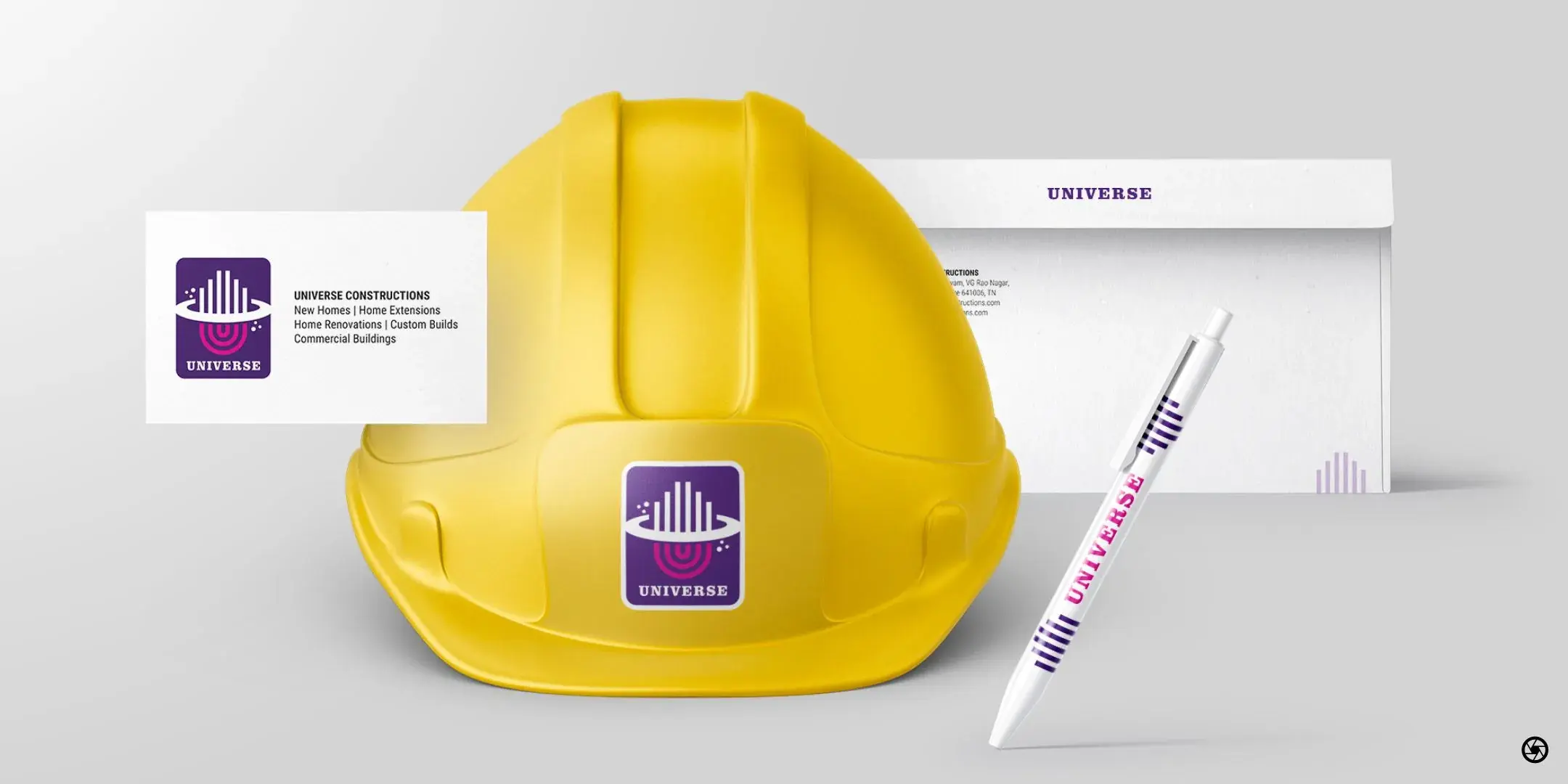 Universe Constructions - composition with the yellow hard hat carrying the brand decal alongside the envelope, business card, and branded pen